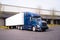 Dark blue big rig semi truck with trailer in warehouse dock load