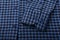 Dark blue and black checkboard pattern shirt fabric background, garment texture with sleeve and buttons, close up