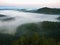 Dark blue fog in deep valley after rainy night. Rocky hill bellow view point. The fog is moving between hills and peaks of trees.