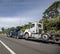 Dark blue powerful mobile big rig towing semi truck tow broken semi truck running on the wide highway road