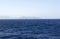 Dark blue sea against a background of blue sky and barely visible mountains on the horizon.