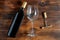 A dark bottle of wine next to a corkscrew and a twisted cork, glass goblet on a wooden background