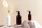 Dark brown cosmetics amber glass bottles on podiums and vase of dried flowers on beige background. SPA bathroom shampoo bottles,