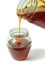 Dark chestnut honey dripping from a large glass jar in the smaller glass jar