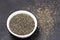 Dark Chia seeds in a white bowl on a black stone background. small grains of Spanish sage