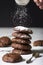Dark chocolate chip cookies on a pile, sifting powdered sugar on the top.
