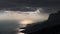 Dark clouds with sunbeams over  sea near rocky coasts at sunset, time lapse