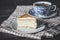 On a dark countertop, on a light checkered linen napkin, a white and blue patterned tea pair with tea and saucer with a piece of