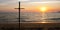 Dark cross at beach as the sun sets over the sea. Cross symbol over the setting sun. Sunset at the beach