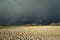 Dark dangerous cloud coming over a plowed field, forest on the horizon