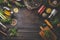 Dark food background with various ingredients and jars with preserved vegetables, seasoning and kitchen tools for tasty home