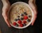 Dark food photography. Plate with porridge in hand on dark background, top view. Healthy Breakfast with raspberries and