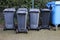 Dark garbage cans are standing at the fence in a row