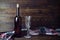 Dark glass wine bottle without label, empty transparent wineglass and colored cloth on brown wooden board background.