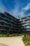 Dark and glassy facade of modern block of flat at new estate with green square around and cafes