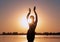 Dark glowing silhouette of slim woman with hands up near big river