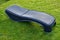 Dark gray plastic deck chair of round shapes with a folding backrest on a mown English lawn in the garden. plastic surface with a