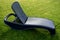 Dark gray plastic deck chair of round shapes with a folding backrest on a mown English lawn in the garden. plastic surface with a