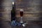 Dark green bottle with cork, transparent wineglass with red wine and bunch of grapes on brown wooden plank background