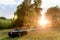 Dark green convertible on a summer meadow with trees leading to sun