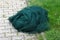 Dark green plastic protection net left on stone tiles next to uncut grass waiting to be used in local garden as protection against