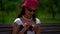 A dark-haired curly-haired young girl is in a summer Park. She wears large white beads, a lilac beret on her head, and