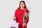 Dark haired dissatisfied woman frowns face, doesnt like present, holds gift bag in one hand and bouquet of flowers in other,