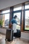 Dark-haired female standing with suitcase, unlocking glass door, leaving