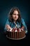 Dark-haired girl on a diet looks at a chocolate cake, struggling with the desire to eat it