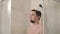 Dark haired man is relaxing in a shower in evening, standing under water flows