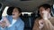 Dark-haired man in sweater and brunette woman in shirt and coat sing and dance listening to loud music sitting in car