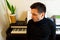 A dark-haired tanned young guy wearing a black turtleneck sitting on background of piano