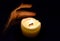 In the dark, a hand reaches for a burning candle. The faint light of the candle illuminates the hand. Hand and candle in