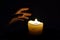 In the dark, a hand reaches for a flame candle. The warmth of the candle warms the skin. The faint light of the candle