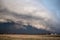 A dark, and menacing storm cloud races across flat farmland bringing dangerous wind and heavy rain.