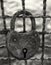 Dark monochrome close up of an old rusty padlock on a corroded metal fence against a blurred outdoor background