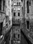 Dark monochrome image of a quiet narrow canal in venice surrounded by picturesque ancient buildings reflected in the water