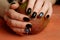 Dark nail art on manicured hands on red background