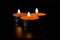 Dark night background, composition of three candles. Black table, side view. Candles Burning at Night. Orange taper burning in