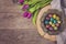 Dark photo of Easter quail eggs in an ancient metal bowl. Beautiful spring flowers - purple tulips on a wooden background. Floral