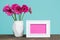 Dark pink gerberas in a vase on a table with empty picture frame greeting card.