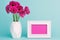 Dark pink gerberas in a vase on a table with empty picture frame greeting card. Happy Mother`s Day, Women`s Day or Birthday