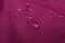 Dark pink waterproof fabric with water drops as background, closeup