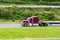 Dark red big rig bonnet classic American semi truck with empty flat bed semi trailer driving on highway to warehouse for pick up