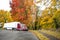 Dark red big rig semi truck tractor with dry van semi trailer standing on the city street parking with autumn trees