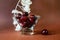 Dark red cherry in glass bowl, dried lunaria flower on brown