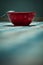 A dark red cup with a metal boat on a checkered tablecloth against a blue wall in the morning ,morning light cold tone, blue