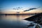 Dark rock dam in blue ocean on twilight sunset and wooden bridge