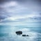 Dark rocks in a blue ocean under cloudy sky in a bad weather.