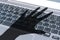 Dark shadow of a hand reaches for computer keyboard symbolizing cyber crime